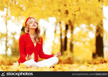 Beautiful young woman sitting in autumn park in lotus yoga position