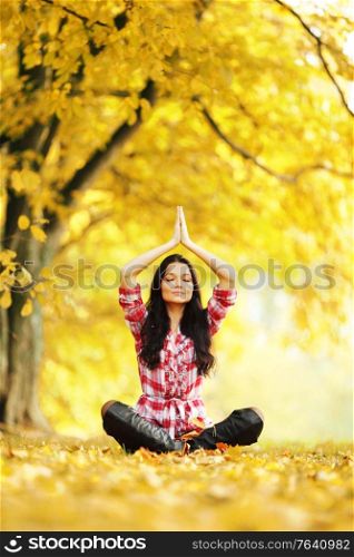 Beautiful young woman sitting in lotus yoga position in autumn park. Autumn yoga woman