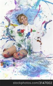 Beautiful young woman sitting in paint covered studio. Paint splattered on walls, floor, model. Shot in studio over &acute;white&acute;. :)