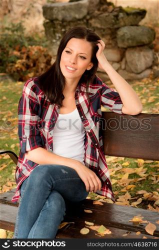 Beautiful young woman sitting on a bench in park at fall