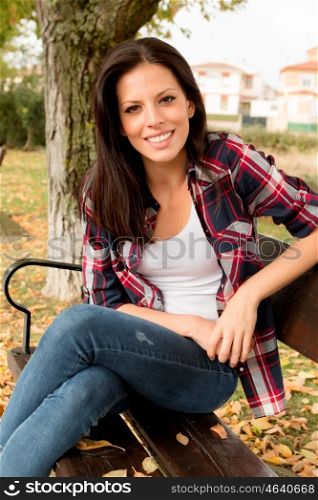 Beautiful young woman sitting on a bench in park at fall