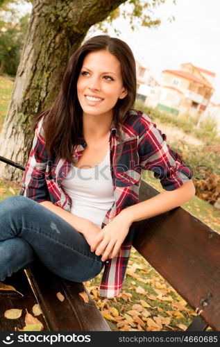 Beautiful young woman sitting on a bench in park at fall