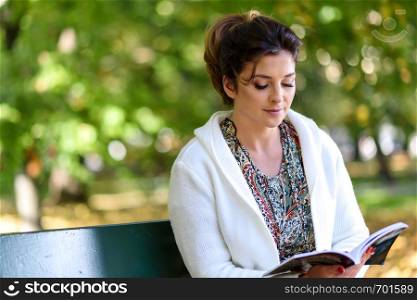 Beautiful young woman sitting on a bench in the park and reading a book on a sunny autumn day.