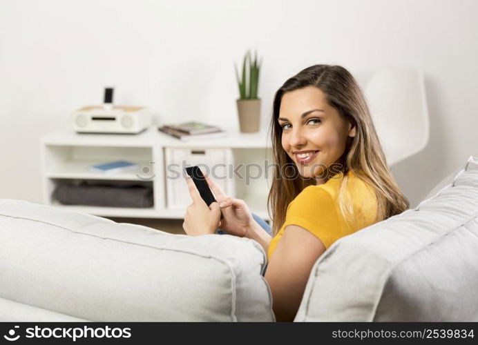 Beautiful young woman sitting on a sofa and send text messages