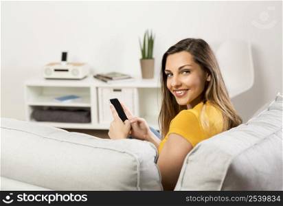 Beautiful young woman sitting on a sofa and send text messages