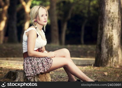Beautiful young woman sitting on a trunk of a tree