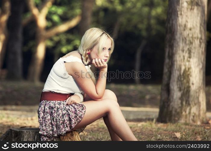 Beautiful young woman sitting on a trunk of a tree and thinking on something