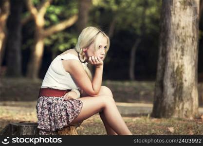 Beautiful young woman sitting on a trunk of a tree and thinking on something