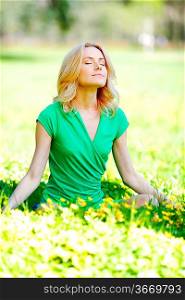 Beautiful young woman sitting on flower field in lotus pose