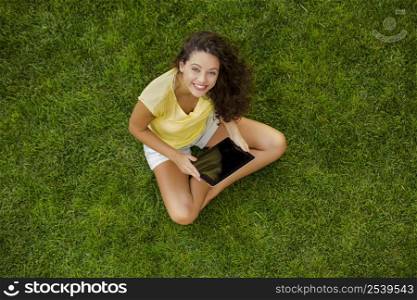 Beautiful young woman sitting on the grass and holding a tablet