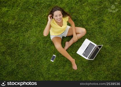 Beautiful young woman sitting on the grass and working with a laptop
