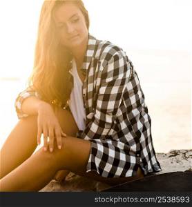Beautiful young woman sitting on the rocks and relaxing at the sunset.