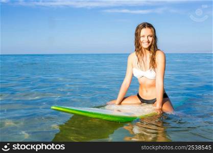 Beautiful young woman sitting on the surfboard and waiting for the waves
