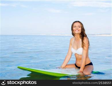 Beautiful young woman sitting on the surfboard and waiting for the waves