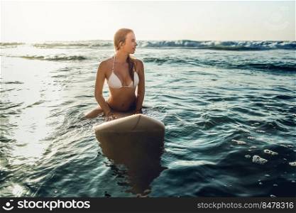 Beautiful young woman sitting on the surfboard waiting for set of waves