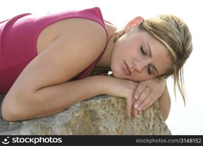 Beautiful young woman sleeping outside on a large rock.