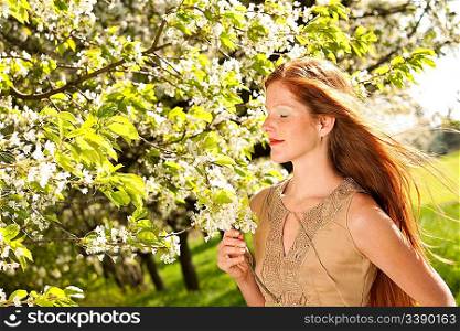 Beautiful young woman smelling cherry tree blossom on a sunny day
