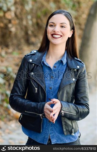Beautiful young woman, smiling in urban background. Girl wearing leather jacket and blue shirt