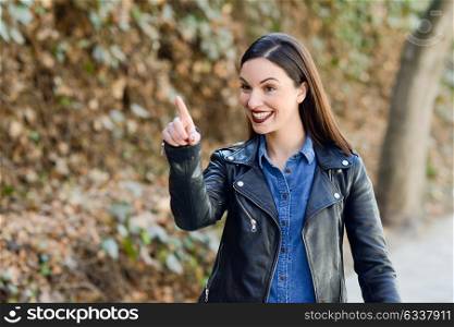 Beautiful young woman, smiling in urban background. Girl wearing leather jacket and blue shirt