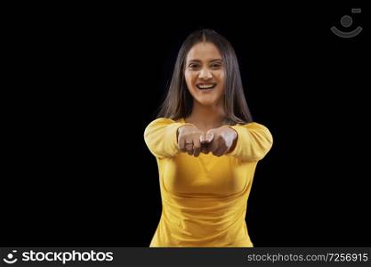 Beautiful young woman smiling pointing at camera over black background