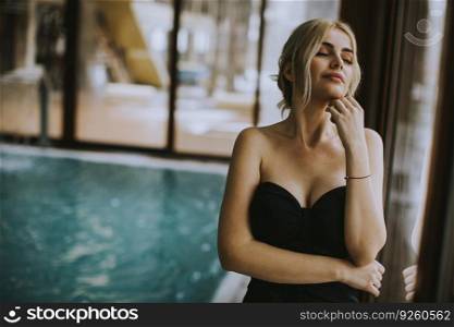 Beautiful young woman standing by the window at indoor swimming pool in spa