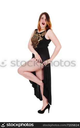 Beautiful young woman standing in a long black evening dress showing her nice leg, isolated for white background