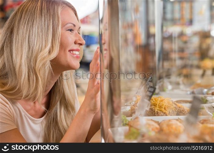 Beautiful young woman standing near supermarket showcase full of different products and showing how she wants something