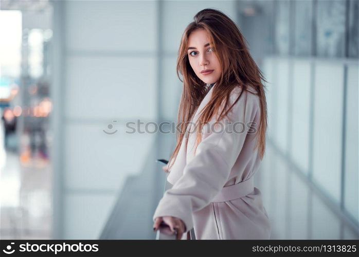 Beautiful young woman standing on glazed balcony at airport terminal. Blur terminal on the background.