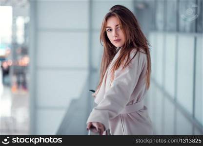 Beautiful young woman standing on glazed balcony at airport terminal. Blur terminal on the background.