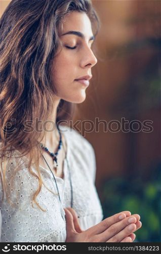 Beautiful young woman standing with her eyes close, meditate while practicing Yoga with hands in prayer position.