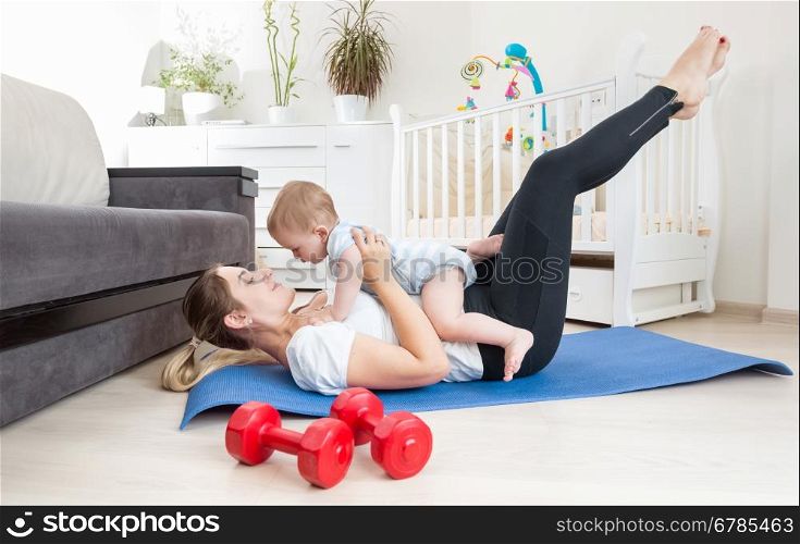 Beautiful young woman stretching on floor and holding her baby boy