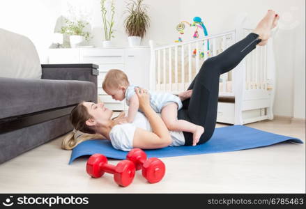 Beautiful young woman stretching on floor and holding her baby boy