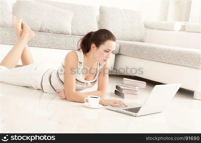 Beautiful Young Woman Student Surfing the Internet Online on Laptop, Drinking Coffee, Lying on the Floor in Living Room