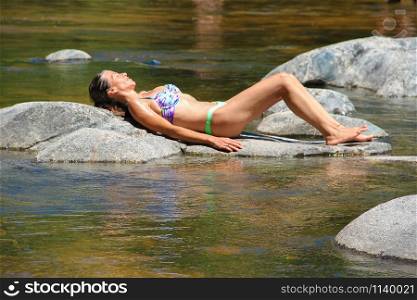 beautiful young woman sunbathing on the rocks of the mountain river
