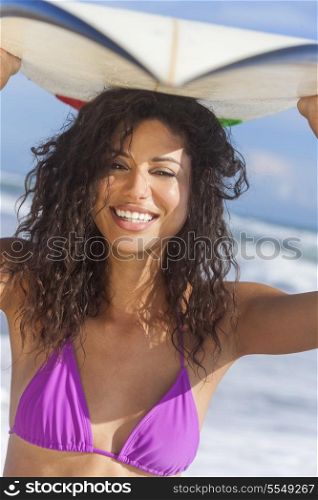 Beautiful young woman surfer girl in bikini with surfboard on her head standing in the surf on a beach