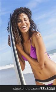 Beautiful young woman surfer girl in bikini with surfboard standing in the surf on a beach