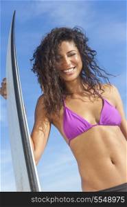 Beautiful young woman surfer girl in bikini with surfboard standing on a beach
