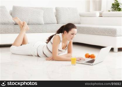 Beautiful Young Woman Surfing the Internet Online on Laptop, Orange Juice, Lying on the Floor in Living Room