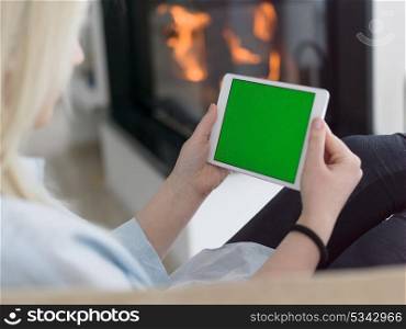 beautiful young woman surfing web using tablet computer in front of fireplace on cold winter day at home
