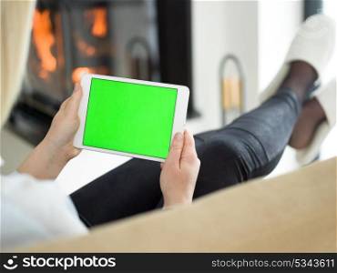 beautiful young woman surfing web using tablet computer in front of fireplace on cold winter day at home