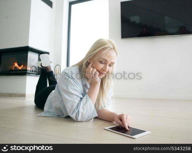 beautiful young woman surfing web using tablet computer on the floor in front of fireplace on cold winter day at home