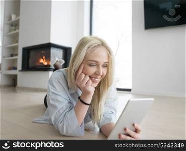 beautiful young woman surfing web using tablet computer on the floor in front of fireplace on cold winter day at home