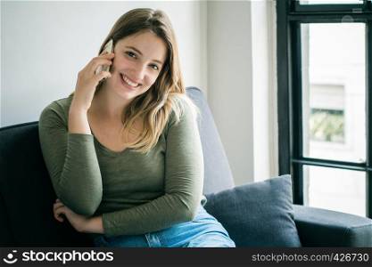Beautiful young woman talking on phone and relaxed on couch. Indoors.