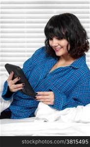 Beautiful young woman texting in bed on her tablet