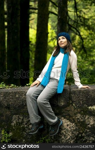 Beautiful young woman thinking on something while sitting on a stonewall