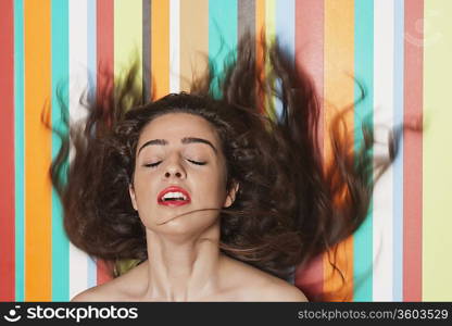 Beautiful young woman tossing hair against colorful striped background