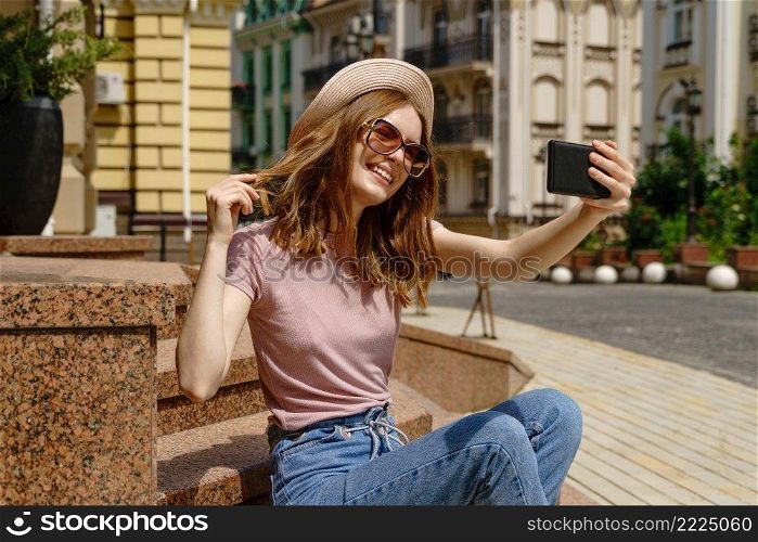 Beautiful Young Woman tourist sitting on stairs using smartphone making video call or selfie.. Beautiful Young Woman tourist sitting on stairs using smartphone making video call or selfie