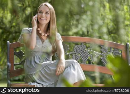 Beautiful young woman using cell phone on bench in park