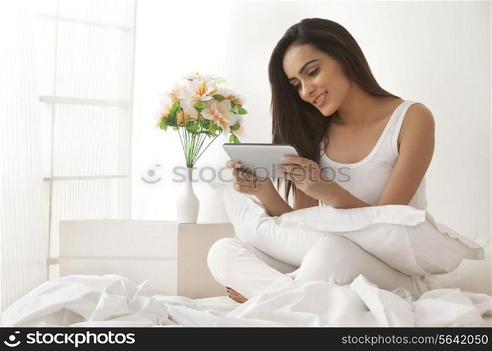 Beautiful young woman using digital tablet on bed