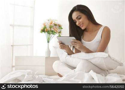 Beautiful young woman using digital tablet on bed